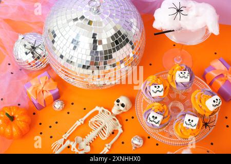 Halloween-Party-Komposition mit Cupcakes, Disco-Ball, Getränk und Deko auf orangefarbenem Tisch Stockfoto
