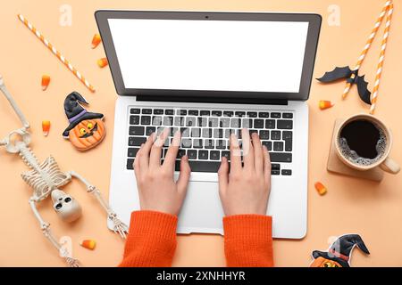Weibliche Hände mit Laptop-, Kaffee- und Halloween-Deko auf beigem Hintergrund Stockfoto