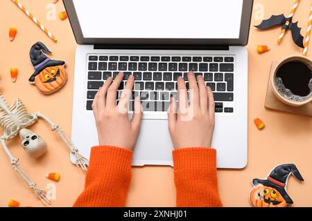 Weibliche Hände mit Laptop-, Kaffee- und Halloween-Deko auf beigem Hintergrund Stockfoto