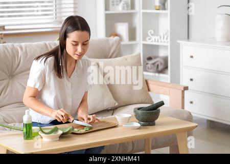 Schöne junge Frau, die Aloe Vera im Wohnzimmer schneidet Stockfoto