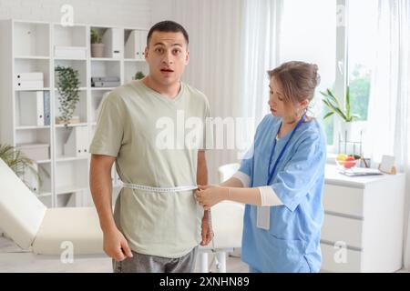 Ärztin, die die Taille des Mannes in der Klinik misst Stockfoto