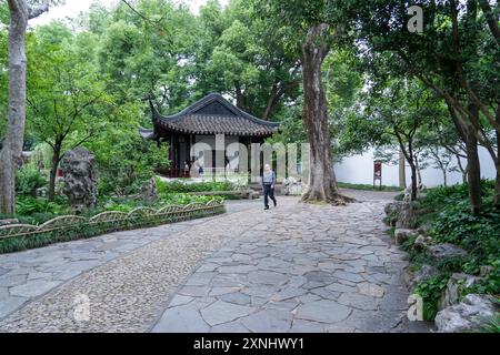 Suzhou, China - 11. Juni 2024 : Ein Steinweg führt durch einen üppigen chinesischen Garten zu einem traditionellen Pavillon. Stockfoto