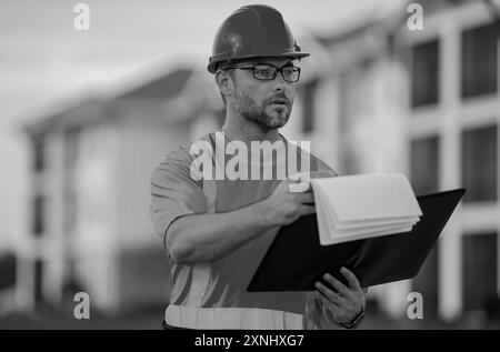 Bauarbeiter vor Ort. Arbeiter mit Schutzhelm. Bauarbeiter im Helm beim Bau eines neuen Wohngebäudes. Ingenieur mit Zwischenablage Stockfoto