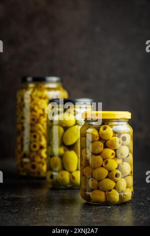 Eingelegte grüne Oliven in Salzlake im Glas auf einem schwarzen Tisch. Stockfoto