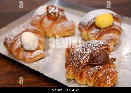 Auf dem Tablett liegen frisch gebackene Croissants mit verschiedenen Füllungen und mit Puderzucker überzogen Stockfoto