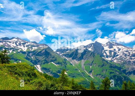 Österreichische Alpen mit schneebedeckten Berggipfeln und grünen Hängen vor blauem Himmel mit Wolken. Stockfoto