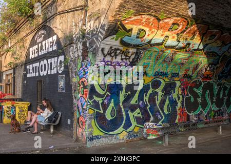 Ein Paar, das sich bei einem Drink vor einem stark begrabenen Eisenbahnbogen in Peckham, London, SE15, entspannt. Stockfoto