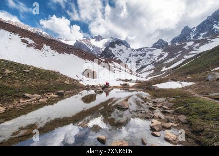 Eine kleine Figur eines Mädchens spiegelt sich im Wasser eines Gletschersees vor dem Hintergrund schneebedeckter Berge und eines blauen Himmels. Stockfoto