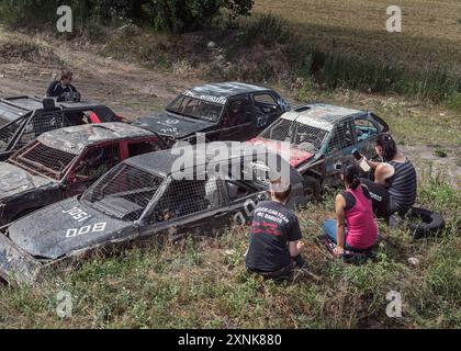 Freunde, die ein intensives Abriss-Derby-Rennen beobachten, sitzen in einer ländlichen Umgebung zwischen alten Stock Cars. Konzept von Spannung und Abenteuer. Stockfoto