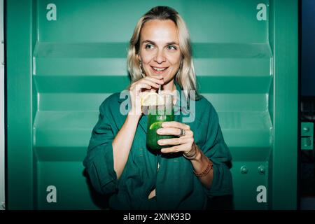 Glückliche Frau mit einem Glas kühlem Sommerfest-Drink in einer Bar. Hochformat mit Blitz. Stockfoto