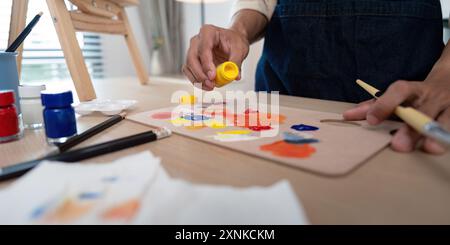 Künstler mischt Farben auf Palette im Studio mit Pinseln und Staffelei im Hintergrund Stockfoto