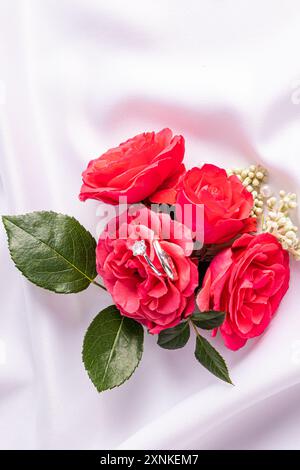 Zwei schicke Diamant-Eheringe liegen in den Blütenblättern eines Rosenstraußes. Blick von oben. Vertikaler Hochzeitshintergrund. Postkartenvorlage Stockfoto