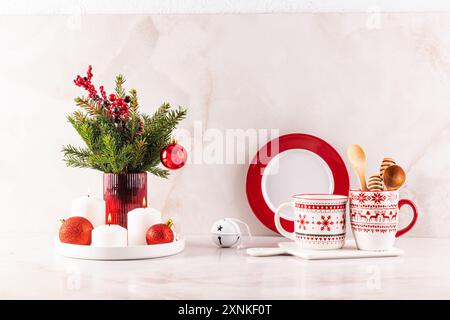 Zwei stilvolle weiße Keramikbecher mit rotem Weihnachtsschmuck in einer festlichen Komposition von Hausdekorationen für die Feiertage. Vorderansicht Stockfoto