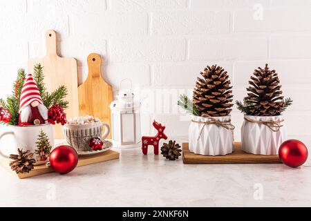 Zwei große Zedernkegel in einem festlichen Pflanzgefäß, ein Neujahrsgnome zwischen den Zweigen einer Fichtenbäume, Kegel auf der Küchenarbeitsplatte. Weihnachtsküche Stockfoto