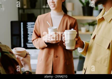 Gruppe nicht erkennbarer junger Menschen, die wiederverwendbare Tassen halten und Kaffeepause am Arbeitsplatz haben Stockfoto