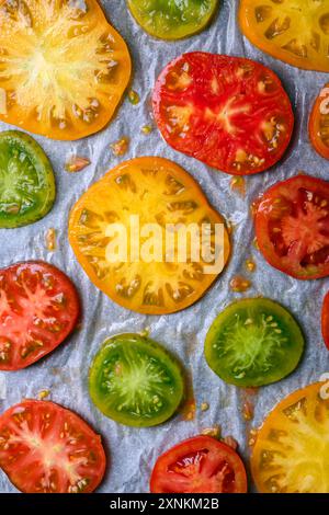 Tomatenscheiben verschiedener Art und Farben vor dem Backen im Ofen. Draufsicht. Nahaufnahme, wie man gebratene Tomaten zubereitet Stockfoto