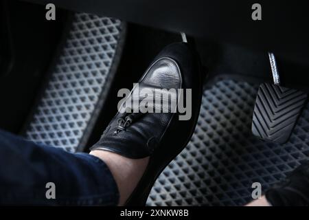 Mann in schwarzen Schuhen, der auf das Pedal der Autobremse drückt, Nahaufnahme Stockfoto