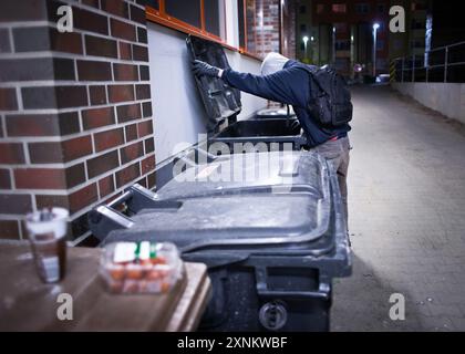 Eine Person, die nachts in Mülltonnen tauchte und verwertbare Lebensmittel und Produkte aus den Abfalltonnen des Supermarkts in Berlin sammelte. Stockfoto