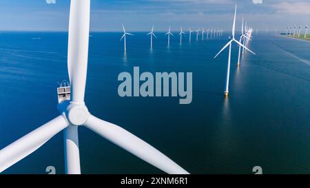 Majestätische Windturbinen stehen hoch über dem glitzernden Wasser der Niederlande und erzeugen unter einem klaren blauen Himmel saubere Energie. Stockfoto