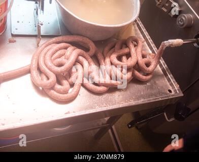 Nahaufnahme von frisch zubereiteten Würstchen, die auf einer Edelstahloberfläche in einer gewerblichen Küche zubereitet werden. Zeigt den Prozess der Wurstherstellung und hebt die verwendeten Rohzutaten und Geräte hervor. Stockfoto