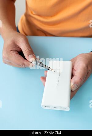 Nahaufnahme der Hände, die die weiße Powerbank mit einem Schraubendreher auf blauem Hintergrund reparieren Stockfoto