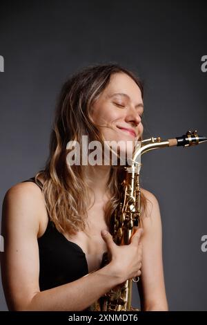 Glückliches weißes Mädchen, das auf der Bühne Jazz-Saxophon spielt Stockfoto