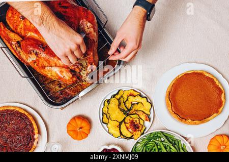 Eine Person schnitzt an einem Thanksgiving-Tisch einen goldbraun gerösteten truthahn mit köstlichen traditionellen Gerichten wie grünen Bohnen, Kürbis und Preiselbeersauce Stockfoto