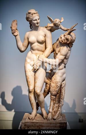 ATHEN, Griechenland – die Marmorskulpturengruppe „Aphrodite, Pan und Eros“ im Archäologischen Nationalmuseum in Athen. Das Kunstwerk aus der hellenistischen Ära, datiert um 100 v. Chr., wurde 1904 auf der Insel Delos entdeckt. Es zeigt Aphrodite, die Pan mit ihrer Sandale abwehrt, während Eros darüber schwebt. Stockfoto