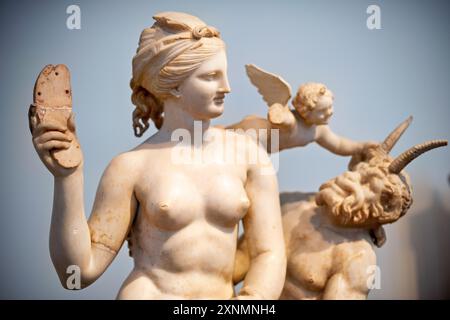 ATHEN, Griechenland – die Marmorskulpturengruppe „Aphrodite, Pan und Eros“ im Archäologischen Nationalmuseum in Athen. Das Kunstwerk aus der hellenistischen Ära, datiert um 100 v. Chr., wurde 1904 auf der Insel Delos entdeckt. Es zeigt Aphrodite, die Pan mit ihrer Sandale abwehrt, während Eros darüber schwebt. Stockfoto