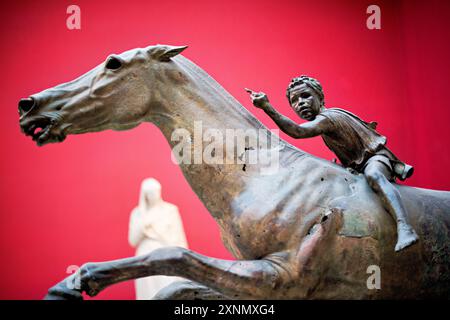 ATHEN, Griechenland — der Jockey von Artemision, eine Bronzeskulptur eines Pferdes reitenden Kindes, ist eine der bemerkenswerten Ausstellungen im Nationalen Archäologischen Museum in Athen. Diese antike griechische Skulptur aus der hellenistischen Zeit (um 150-140 v. Chr.) wurde aus dem Meer vor dem Kap Artemision im Norden Euböas geborgen. Die Skulptur ist bekannt für ihre dynamische Darstellung von Bewegung und Detail, die das künstlerische Können und die Handwerkskunst der antiken griechischen Handwerker veranschaulicht. Stockfoto