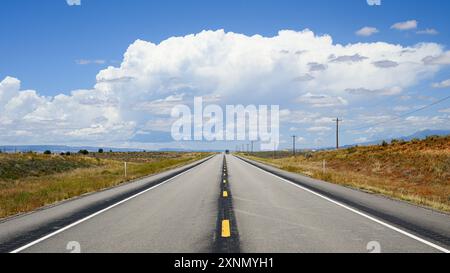 Zweispurige Straße, die offene Hochwüste in Richtung großer weißer Wolke führt Stockfoto