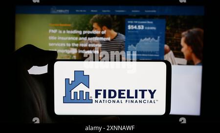 Person, die ein Mobiltelefon mit dem Logo des US-Finanzunternehmens Fidelity National Financial Inc. Vor der Webseite des Unternehmens hält. Schwerpunkt auf dem Display des Telefons. Stockfoto