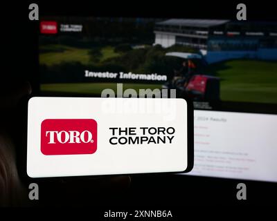 Person, die ein Smartphone mit dem Logo des US-Rasenmähers The Toro Company vor der Website hält. Schwerpunkt auf dem Display des Telefons. Stockfoto