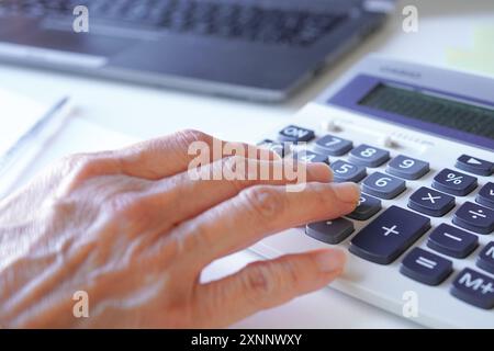 Die Hand einer älteren Beraterin, die Berechnungen an einem Rechner in ihrem Büro durchführt Stockfoto