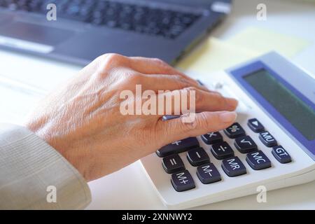 Die Hand einer älteren Beraterin, die Berechnungen an einem Rechner in ihrem Büro durchführt Stockfoto