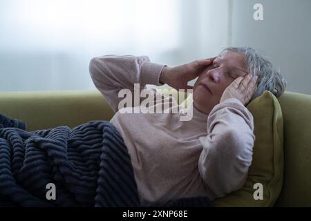 Eine kranke alte Frau, die sich im Bett niederlegte und Migräne hatte. Stockfoto