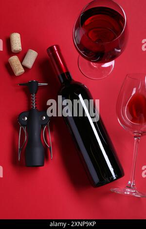 Flügelkorkenzieher, Wein, Gläser und Korken auf rotem Hintergrund, flach Stockfoto