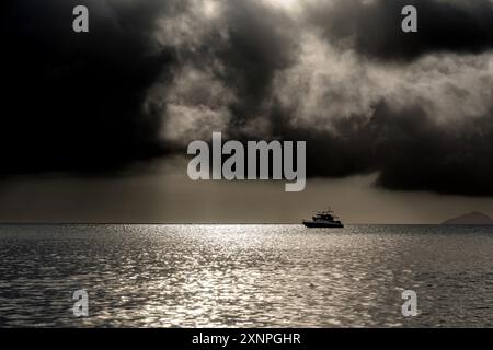 Einsames Fischereischiff im Meer bei Gewitter und massiven schwarzen Wolken am Himmel. Seefahrtsschiffe und malerischer Blick auf die Natur Stockfoto