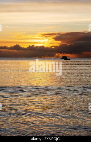 Vertikales Bild mit Fischereischiffen auf dem Meer am Horizont unter den Wolken bei Sonnenuntergang. Seefahrtsschiffe und malerischer Blick auf die Natur Stockfoto