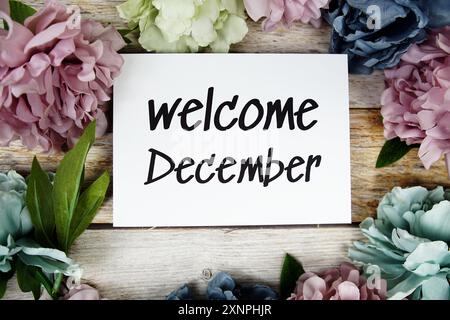 Begrüßungstext im Dezember auf Papierkarte mit Blumenrahmen von oben auf hölzernem Hintergrund Stockfoto