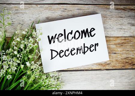 Begrüßungstext im Dezember auf Papierkarte mit Blumenrahmen von oben auf hölzernem Hintergrund Stockfoto