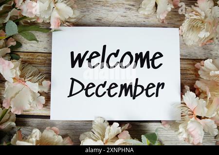 Begrüßungstext im Dezember auf Papierkarte mit Blumenrahmen von oben auf hölzernem Hintergrund Stockfoto