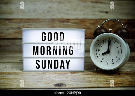 Guten Morgen Sonntag Text auf LED Leuchtkasten mit Wecker auf hölzernem Hintergrund Stockfoto