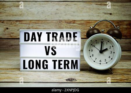Tageshandel im Vergleich zu langfristigem Text auf LED-Leuchtkasten mit Wecker auf hölzernem Hintergrund, Business and Money Konzept Stockfoto