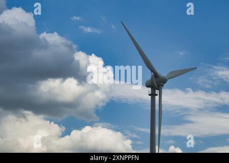 Windkraftanlage steht hoch vor einer Mischung aus bewölktem und klarem blauem Himmel und steht für erneuerbare Energien und Nachhaltigkeit. Stockfoto