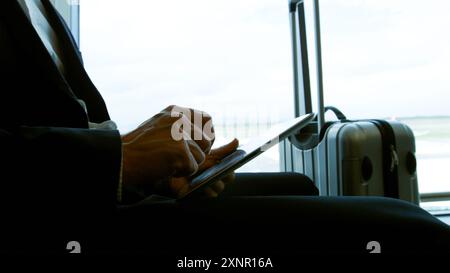 Geschäftsmann Reisender Vor Dem Tablet-Computer Junger Tourist, Der Am Flughafen Sitzt Und Seine Tasche Hält, Wartet Auf Flug, Urlaub Stockfoto