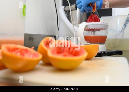 Eine Person, die einen Entsafter verwendet, um Saft aus frischen Früchten zu extrahieren, wobei geschnittene Früchte im Vordergrund stehen. Die Einstellung scheint eine Küche oder eine Zubereitung von Speisen zu sein Stockfoto