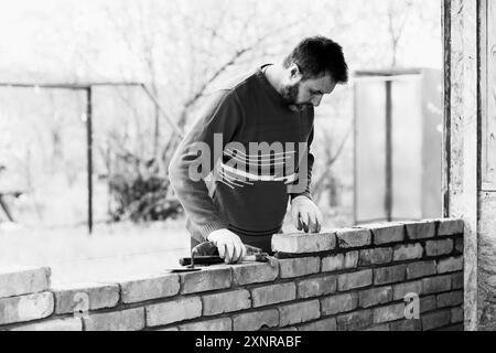 Ein Mann baut eine Mauer aus Ziegeln, legt einen Ziegel auf ein Zementsandmörtel, ein Schwarzweißfoto Stockfoto