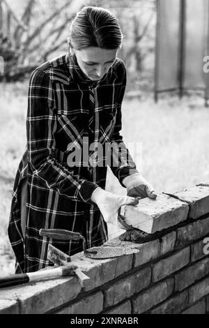 Eine junge Maurerin baut eine Mauer, legt einen Ziegel auf ein schwarzweißes Foto aus Zementmörtel Stockfoto