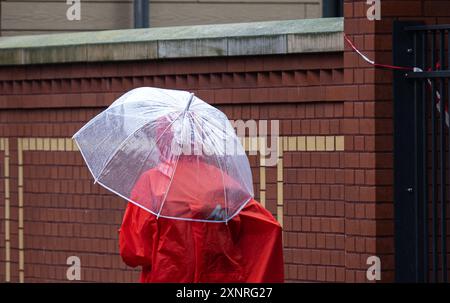 Erfurt, Deutschland. August 2024. Eine Person läuft durch den Regen mit einem Regenschirm und einem regenumhang. Der Deutsche Wetterdienst (DWD) warnt vor starkem Dauerregen in Erfurt. Die Rettungsdienste der Berufsfeuerwehr und der Freiwilligen Feuerwehr sind derzeit in der ganzen Stadt unterwegs. Quelle: Hannes P. Albert/dpa/Alamy Live News Stockfoto